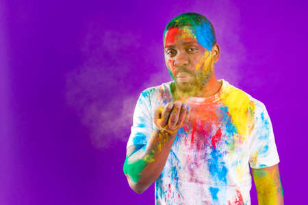 Afro american man celebrate holi festival in violet studio backgroundの写真素材