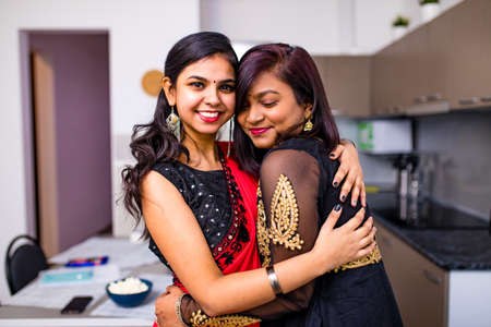 two indian women with bindi on the forehead hugging in living room