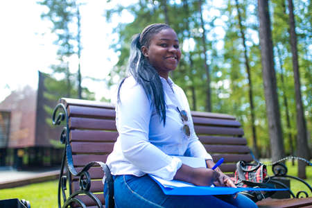 Beautiful smiling young african woman wearing white t-shirt and holding a copybookの写真素材