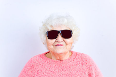 Portrait of funny senior blonde woman in sun glasses and pink sweater on white backgroundの写真素材