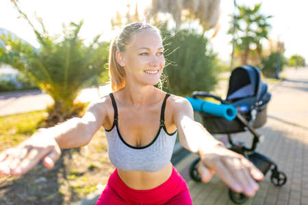 blonde yound mom working out outdoors warming up with yoga mat in tropical beachの写真素材