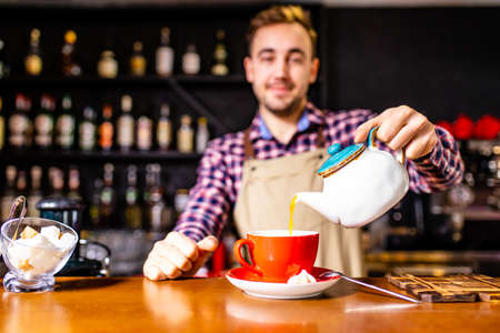 a turkish man in a plaid shirt and apron stands behind a bar and prepare a teaの写真素材