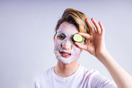 non binary portrait of asian man with luxurious blonde hair and gorgeous make-up in white wall studio background with face moisturizing maskの写真素材