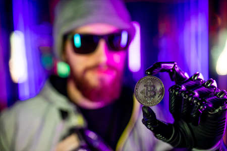 man with prosthetic robot hand holding bit-coin golden in neon background