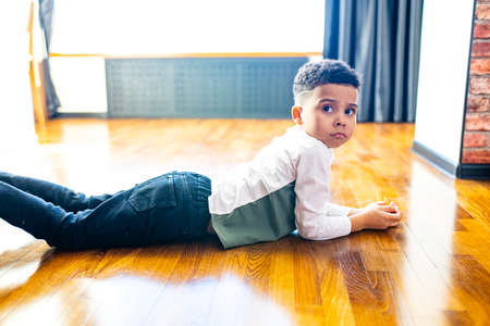 ethnic hispanic curly son sitting on floor warm brown clean safety parquet at homeの写真素材