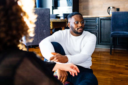 african american thoughtful married man sutting on the floor in front of a woman an looking away in modern apartmentの写真素材