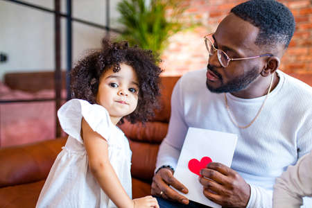 afro american baby giving to dad a Valentines Day picture in living roomの写真素材