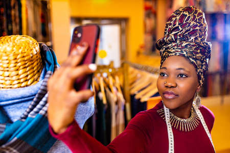 tanzanian woman with snake print turban over hear working in fabrics shop selfie taking on phone cameraの写真素材