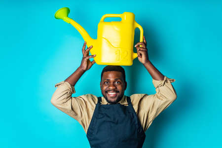 latino spain man in black apron holding yellow watering can in blue studioの写真素材