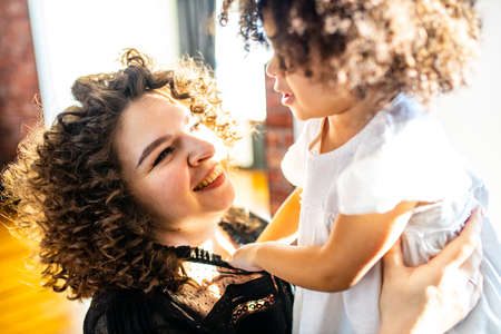 curly hair cute little mixed race baby in mothers hands in cozy room daylightの写真素材
