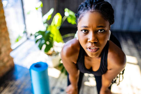 mixed race healthy woman in black sporty suit during her fitness workout at home against the...