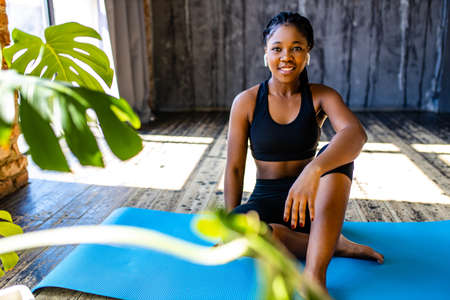 mixed race healthy woman in black sporty suit during her fitness workout at home against the background of panoramic windows sunlightの写真素材