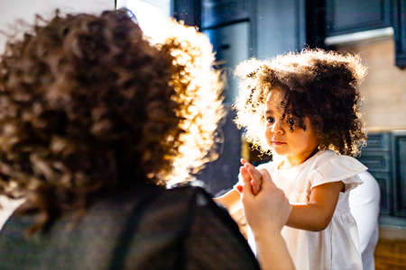 curly hair cute little mixed race baby in mothers hands in cozy room daylightの写真素材