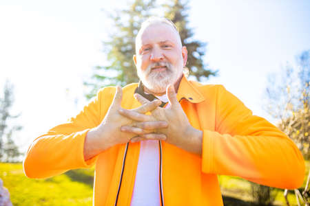 Senior man in orange sports wear doing stretching warming up outdoors sunny day in forest alone