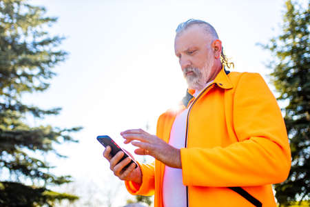 Senior man in orange sports wear doing stretching warming up outdoors sunny day in forest alone