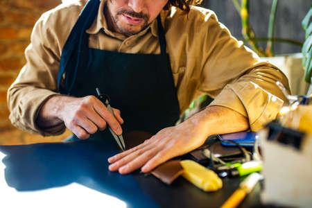 hobby became a small business leather man in apron is making a leather wallet and shooes in studio