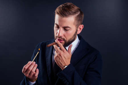 Portrait of an attractive business man with a cigar in black background studioの写真素材