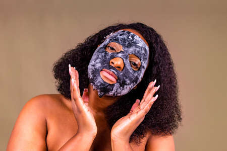 Young woman with bubble sheet mask on her face on brown backgroundの写真素材