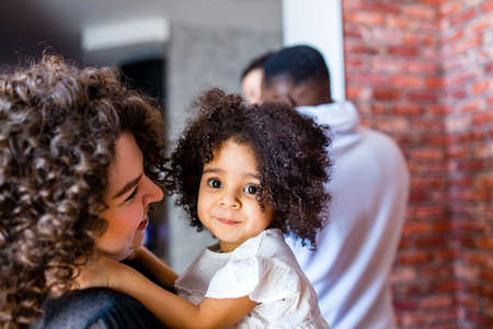 curly hair cute little mixed race baby in mothers hands in cozy roomの写真素材