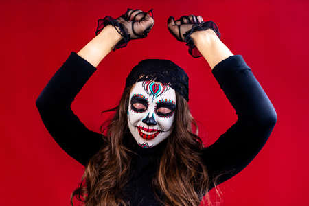 mexican young woman in a costume of Calavera Catrina over red studio background