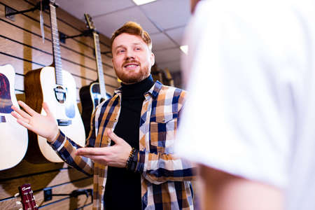 Man with red ginger hair and beatd is considering a guitars in a music storeの写真素材