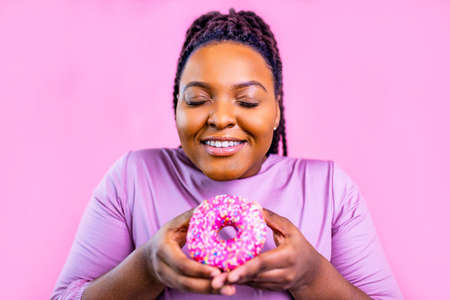 multicultural female holding delicious sweet donut in pink studio backgroundの写真素材