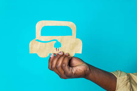 mixed race man holding paper car with recharging socket in blue studio background eco electro car conceptの写真素材