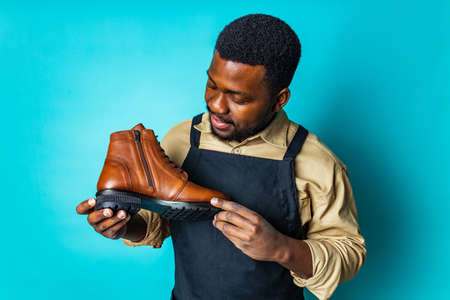 latin hispanic man in black apron showing brown leather shoes in blue studio background