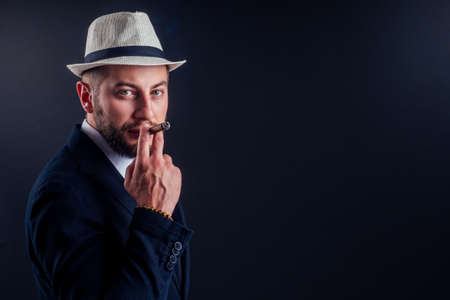 Portrait of an attractive business man with a cigar in black background studioの写真素材