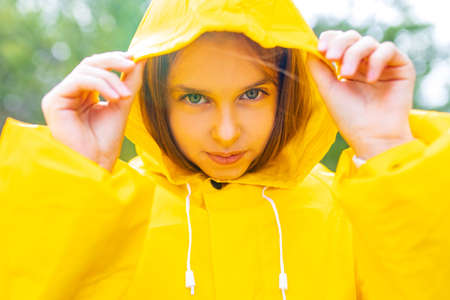 smiling teenage girl wearing raincoat outdoors in rainy dayの写真素材