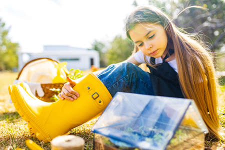 beautiful schoolgirl teenager spending time outdoors in garden wear yellow rubber shoes boots looking into a small glasshouseの写真素材