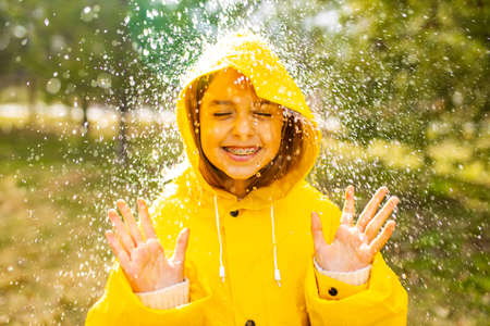 smiling teenage girl wearing raincoat outdoors in rainy dayの写真素材