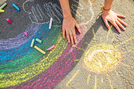 teenage girl drawing a rainbow colored chalk on the asphalt on summer dayの写真素材