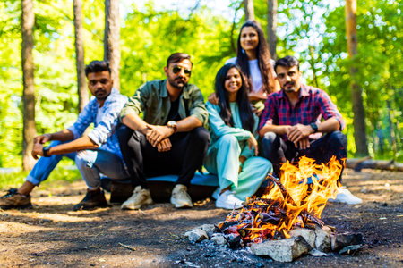 group of five happy mixed race friends frying sausages at forest near campfireの写真素材