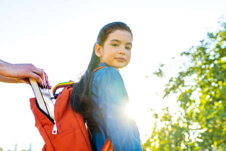 Smiling indian student girl wearing school backpack and blue t-shirt in park