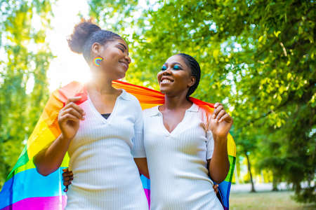 two afro american women celebrating marriage in wtite dress with bright male up in summer park