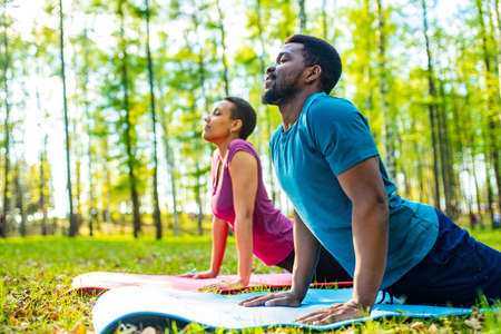 An attractive young woman and man doing yoga in green forestの写真素材
