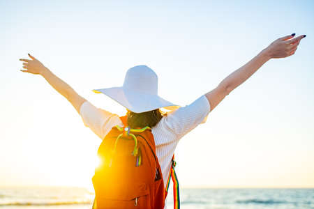 woman with orange backpack with rainbow straps rainbow and hat at sea beach at sunset