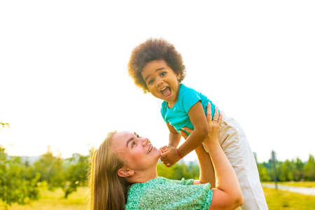 african american little curly girl playing with her mother in summer parkの写真素材