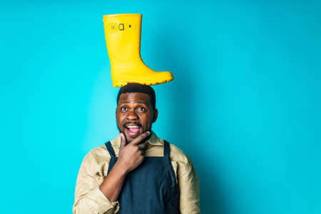 nigerian gardener man showing a yellow rubber shoes in blue studio ready for autumn spring season