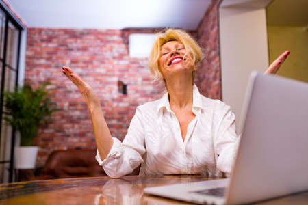 mature lady sitting with laptop in living room at evening lightの写真素材
