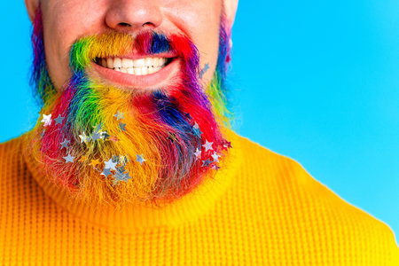 handsome man with raindow in beard with glitter confetti in blue studio baclground