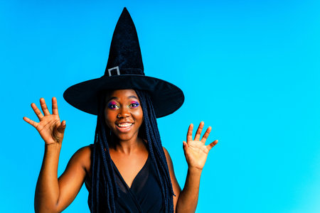 Beautiful young woman in witch costume halloween hat in blue studioの写真素材