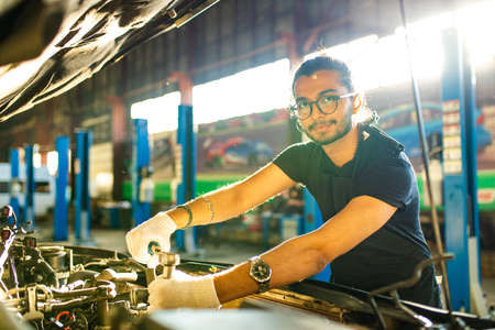latin hispanic auto mechanic in uniform is examining a car while working in auto serviceの写真素材