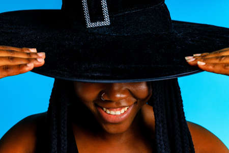 Beautiful young woman in witch costume halloween hat in blue studioの写真素材