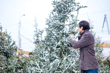 indian man in stylish wool coat buys a Christmas tree outdoors snow backgroundの写真素材