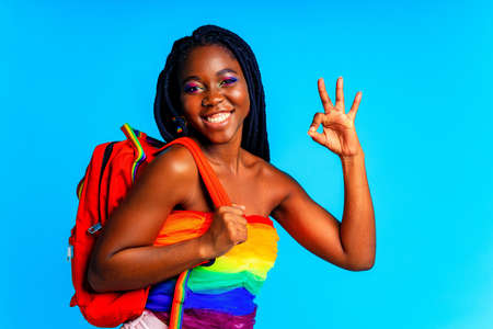 young woman wearing colorful blouse holding backpack isolated over blue background, lgbt conceptの写真素材