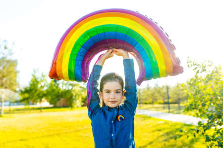 cute little brunette girl holding an air colorful rainbow balloon in summer parkの写真素材