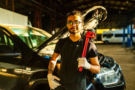 latin hispanic auto mechanic in uniform is examining a car while working in auto service