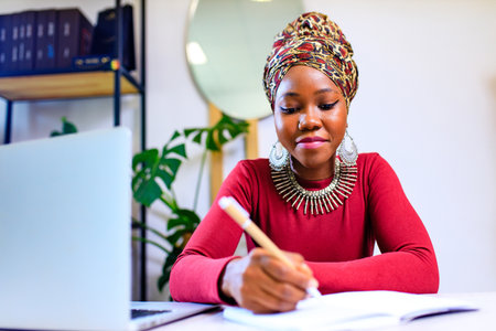 Image of african american woman with turban over head using laptop in officeの写真素材